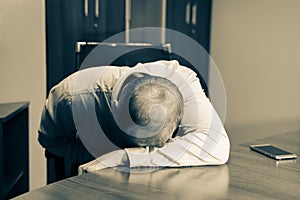  Ill man at desk in office, feeling sick, depressed and exhausted. He is just sitting at working place with his head on the table.