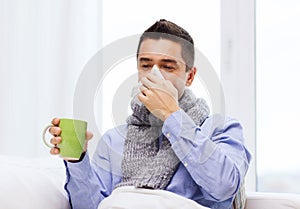 Ill man with flu drinking tea and blowing nose