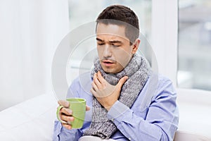 Ill man with flu drinking tea and coughing at home