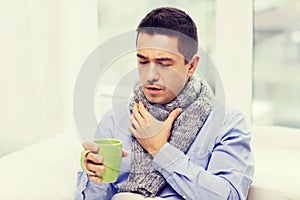 Ill man with flu drinking tea and coughing at home