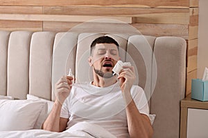 Ill man with nasal spray and paper tissue in bed at home