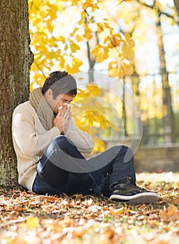 Ill man with paper tissue in autumn park