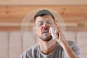 Ill man with paper tissue sneezing at home