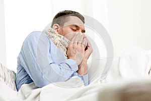 Ill man in scarf blowing nose at home