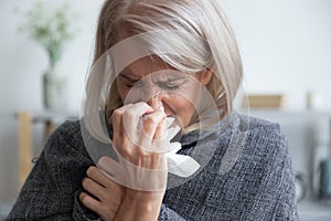 Ill mature woman covered with blanket blowing running nose sneeze