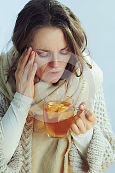 Ill modern woman holding cup of tea and having headache
