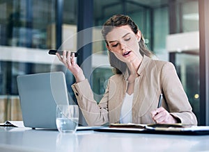 Ill pencil that in my diary right away. a young businesswoman writing notes while using a cellphone in an office.