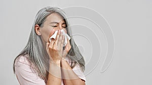 Ill senior woman with cold blowing nose in napkin