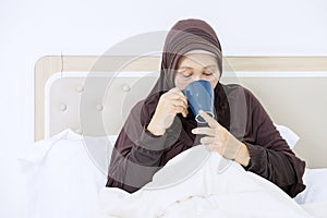 Ill senior woman drinking tea in bedroom