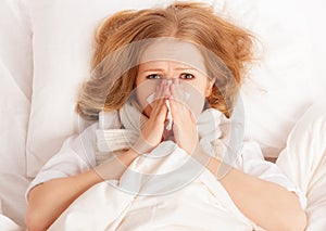 Ill sick young woman sneezes into a handkerchief in bed