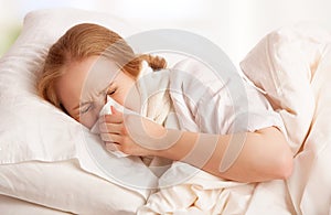 Ill sick young woman sneezes into a handkerchief in bed