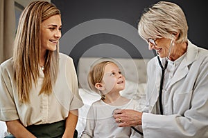 Ill stay by your side. Shot of a doctor examining a little girl and her mother with a stethoscope in bed at home.