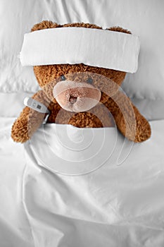 ill teddy bear with bandage and thermometer in bed