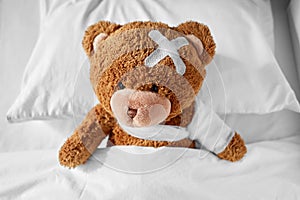 ill teddy bear with bandaged paw and head in bed