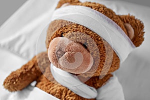 ill teddy bear with bandaged paw and head in bed