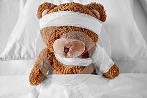 ill teddy bear with bandaged paw and head in bed