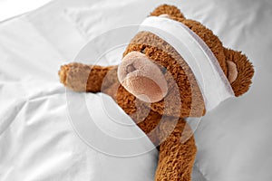 ill teddy bear toy with bandaged head lying in bed