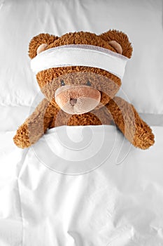 ill teddy bear toy with bandaged head lying in bed