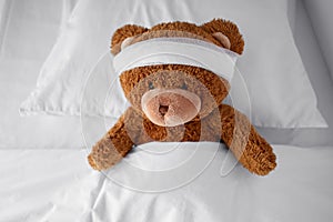 ill teddy bear toy with bandaged head lying in bed