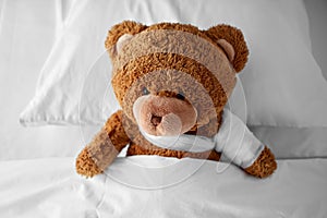 ill teddy bear toy with bandaged paw in bed