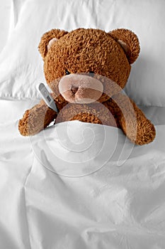 ill teddy bear toy head with thermometer in bed