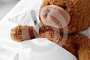 ill teddy bear toy head with thermometer in bed