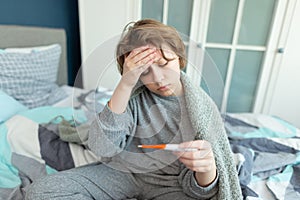 Ill teen with runny nose sitting on a sofa at home and sniffling because of cold and fever. she has to use tissues and take pills