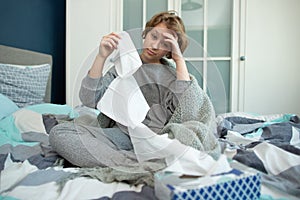 Ill teen with runny nose sitting on a sofa at home and sniffling because of cold and fever. she has to use tissues and take pills