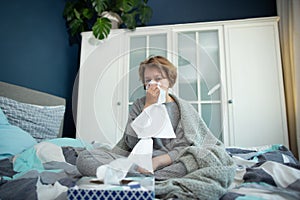 Ill teen with runny nose sitting on a sofa at home and sniffling because of cold and fever. she has to use tissues and take pills