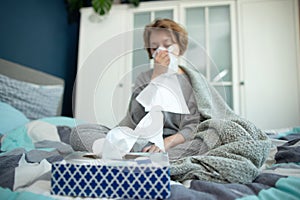 Ill teen with runny nose sitting on a sofa at home and sniffling because of cold and fever. she has to use tissues and take pills