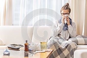 Ill teen with runny nose sitting on a sofa at home and sniffling because of cold and fever. she has to use tissues and take pills photo