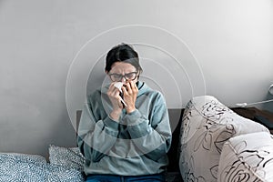 Ill upset young woman sitting on sofa covered with blanket freezing blowing running nose got fever caught cold sneezing in tissue