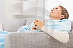 Ill woman with cup of hot beverage sitting on couch