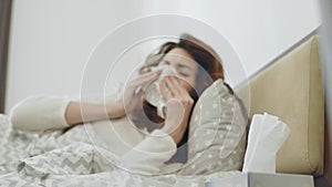 Ill woman getting throat virus lying in bed. Closeup female hands taking napkin