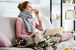Ill woman with grey scarf drinking cough syrup