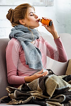 Ill woman with grey scarf drinking cough syrup