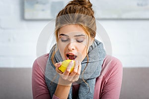 Ill woman with grey scarf eating yellow lemon