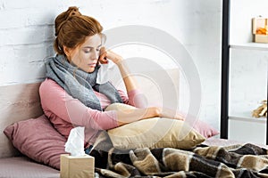 Ill woman with grey scarf sitting in bed and holding napkin