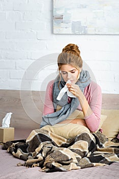 Ill woman with grey scarf sitting in bed and holding napkin