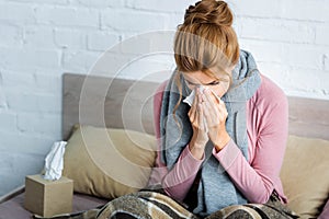 Ill woman with grey scarf sneezing and using napkin