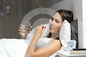 Ill woman looks at you taking pill in the night on the bed