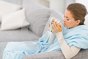 Ill woman sitting on couch with cup of beverage
