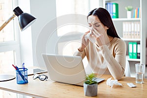 Ill woman sitting at the table with computer at work and using napkin