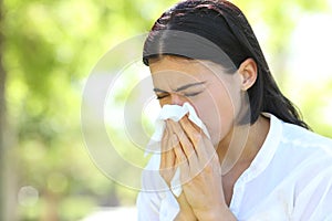 Ill woman sneezing covering mouth with a wipe in a park