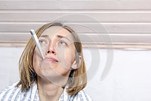 Ill woman with thermometer in mouth on light background. Concept diseases of flu virus, colds, coronavirus