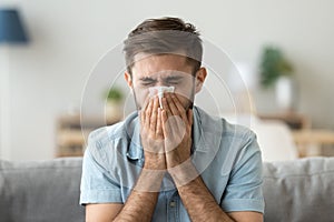 Ill young man sneezing in handkerchief blowing wiping running nose