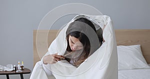 Ill young woman covered with blanket blowing nose got flu