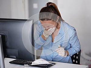Ill young woman using laptop wearing face mask and coughing, working from home or at office, close up
