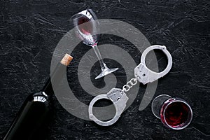 Illegal sale of alcohol concept. Handcuffs near wine glass and bottle on black background top view copy space