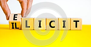 Illicit or elicit symbol. Businessman turns wooden cubes and changes the concept word Illicit to Elicit. Beautiful yellow table